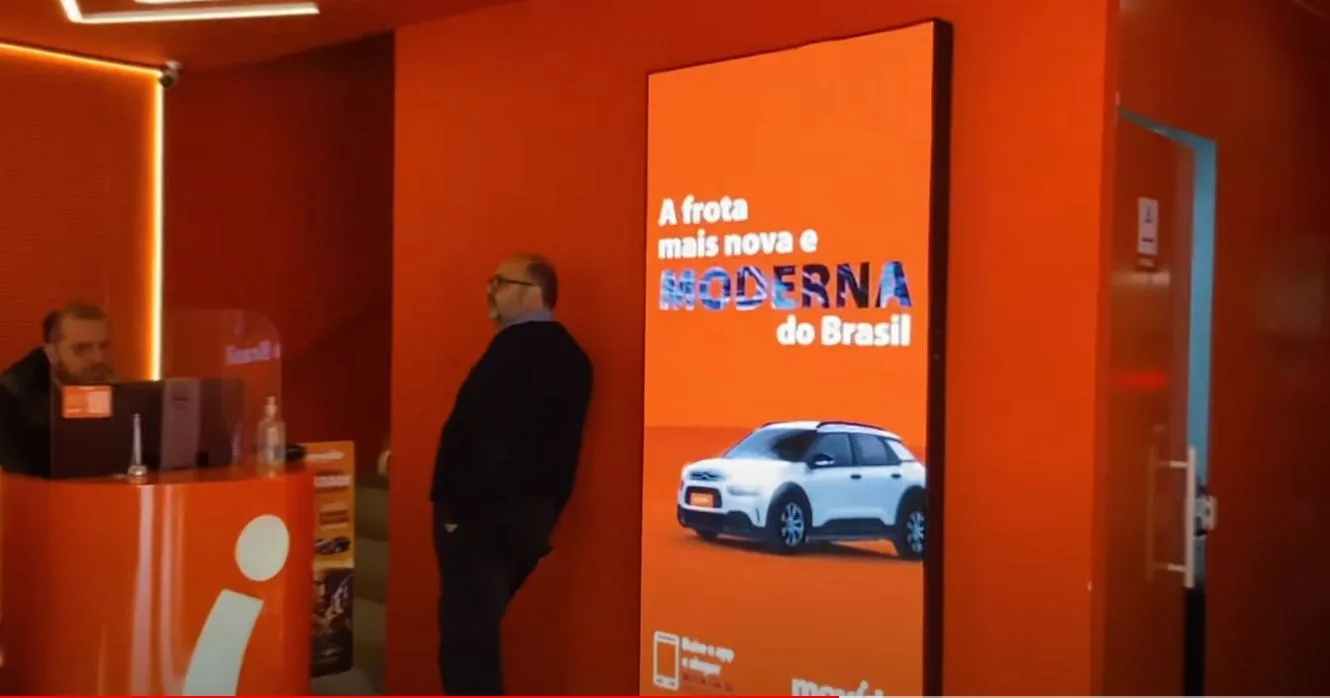 Totem vertical de LED na entrada da agência com campanha da frota
