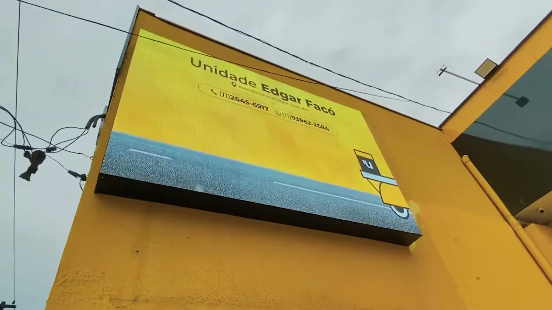 Painel P5 integrado à fachada amarela durante o dia