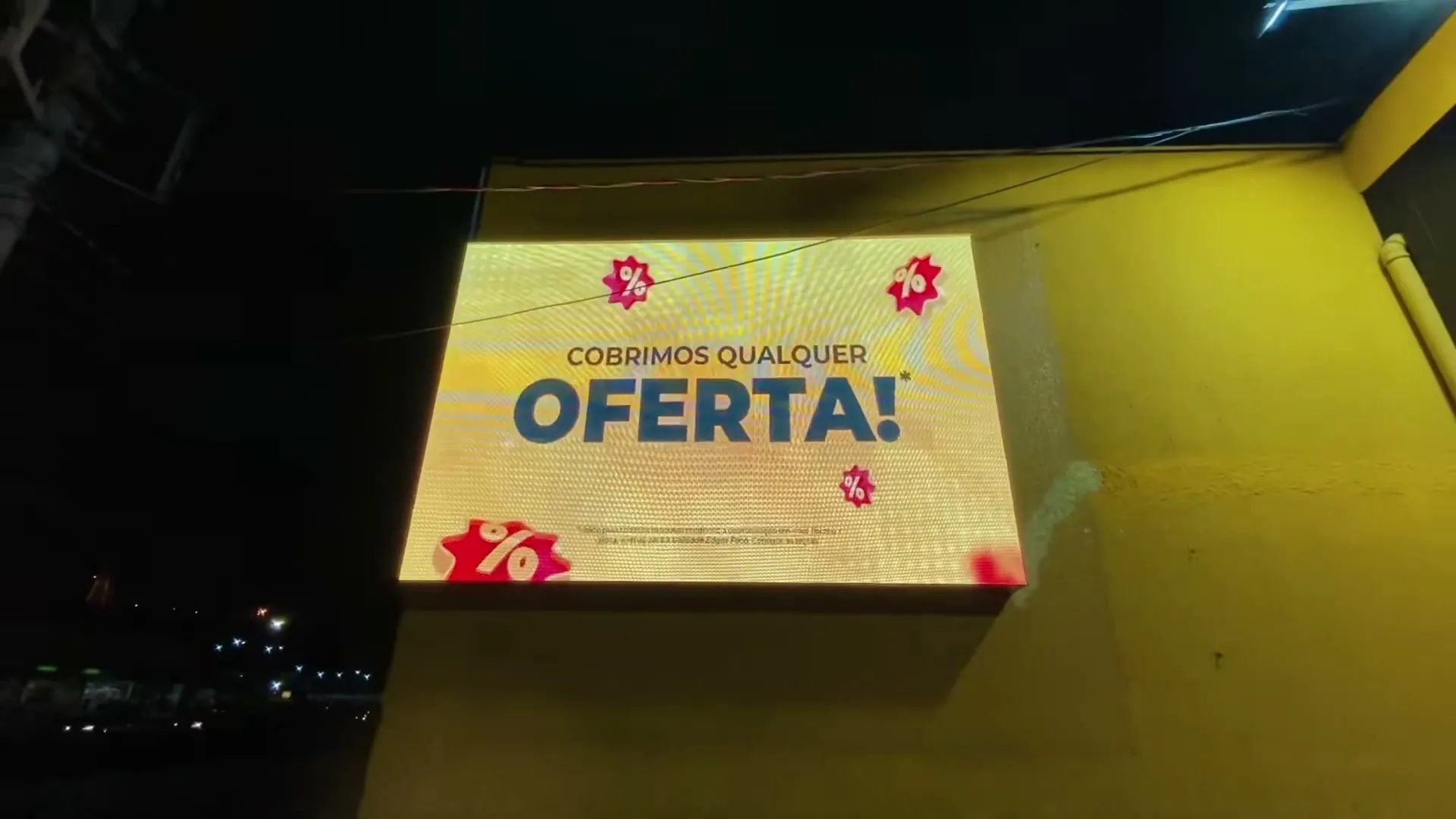 Painel exibindo Cobrimos Qualquer Oferta aceso à noite